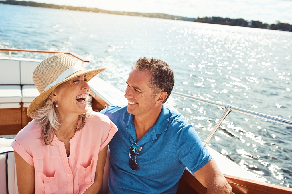 Middle-aged man and woman couple sitting close to each other on a boat smiling and laughing
